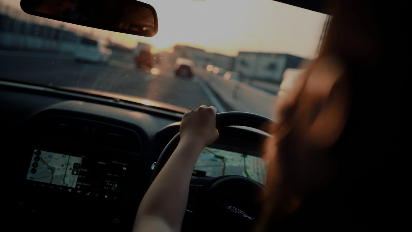 Photo d'une conductrice dans une voiture prise dans son dos. Le volant est à droite et le véhicule se trouve sur une atuto-route japonaise. Traduction permis japonais.